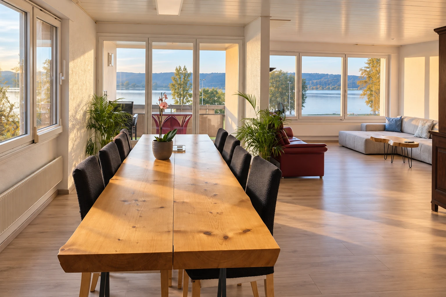 Grande table à manger, salon et baies vitrées ouvertes sur le lac